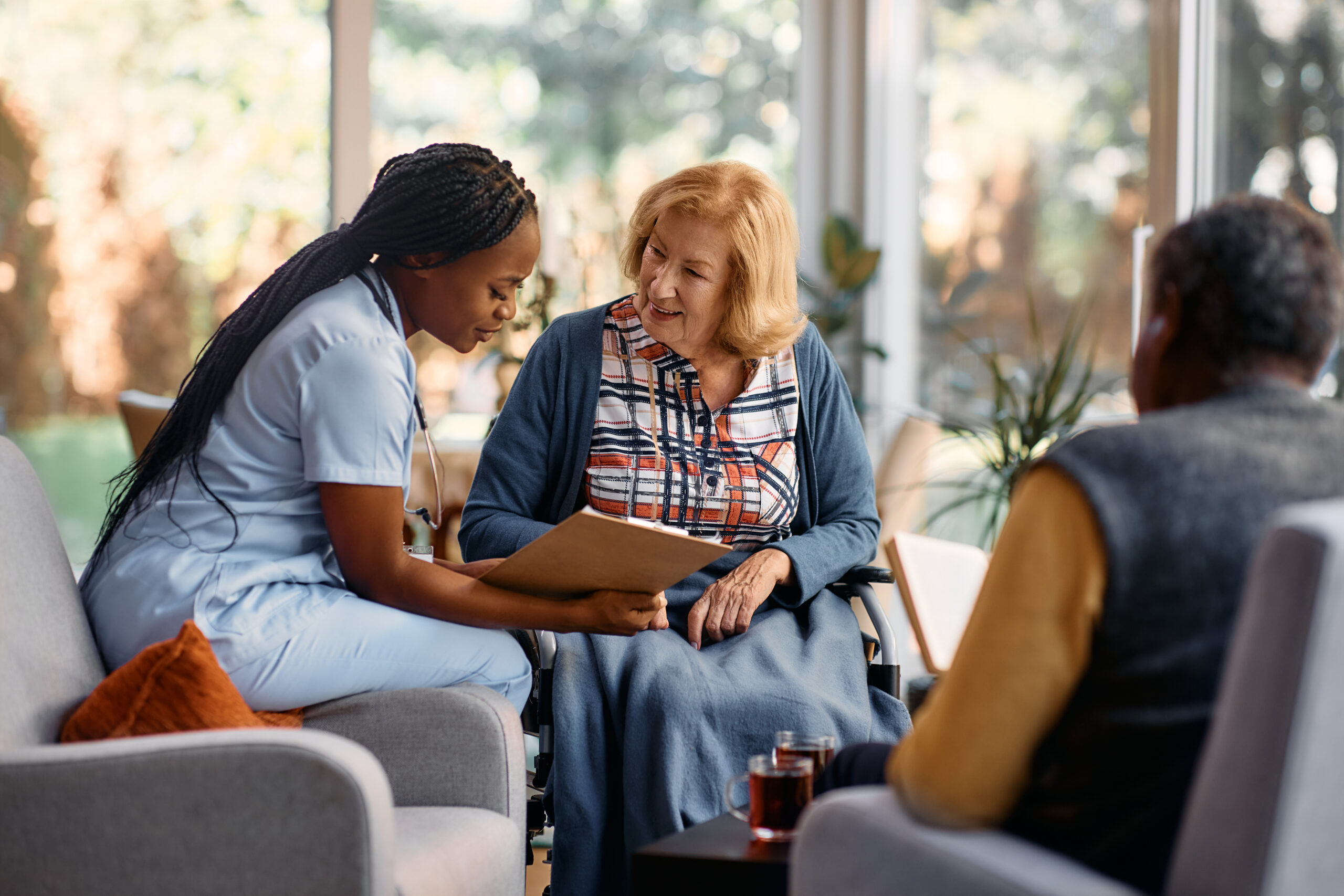 African American nurse analyzing senior woman's medical record while talking to her at nursing home.